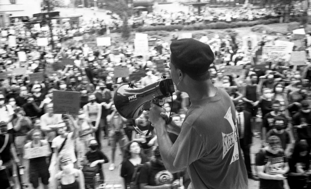 Adrenaline Rush An image of an artwork by Chris Cook depicting a BLM protester standing in front of a crowd with a megaphone
